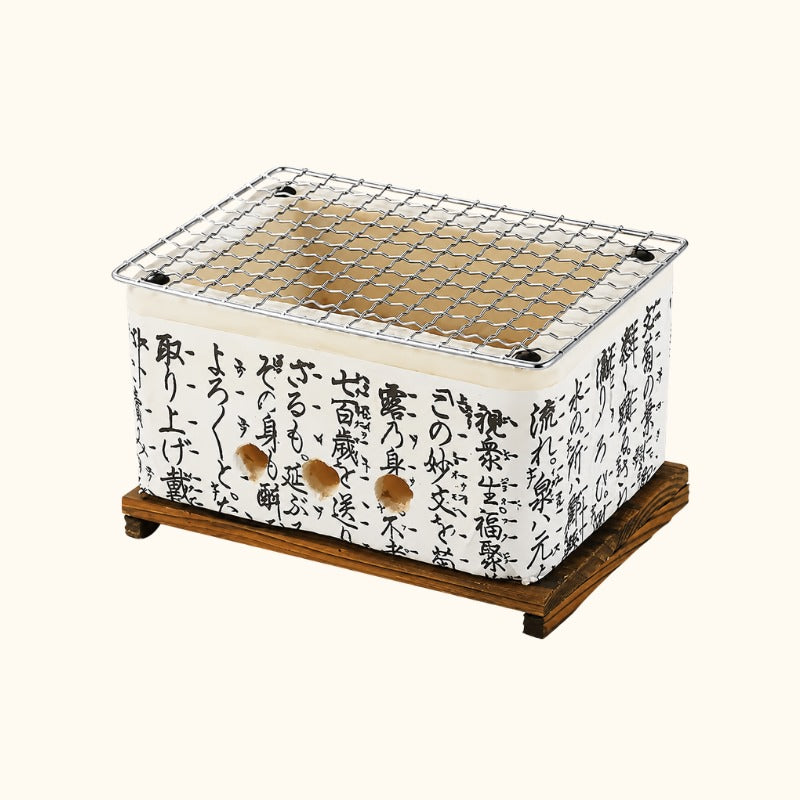 Small Japanese barbecue with white ceramic body covered in black kanji calligraphy and stainless steel mesh grill on a dark wood stand on white background