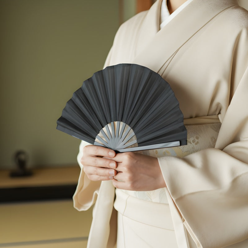 Elegant big japanese fan in black held by person wearing cream kimono in serene traditional interior with warm natural lighting