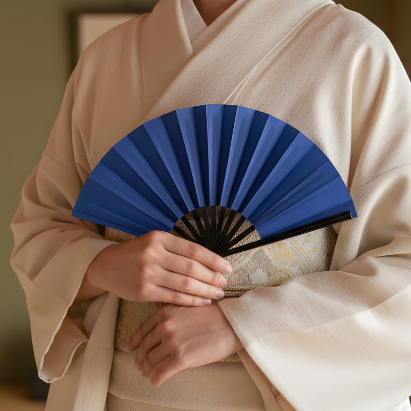 Traditional blue japanese fan held by person in cream kimono with gold obi belt in authentic Japanese interior setting