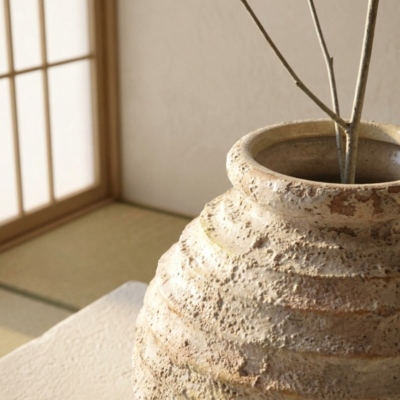 Close up of handmade ceramic vase ikebana showcasing rough striped texture with branches near shoji screen