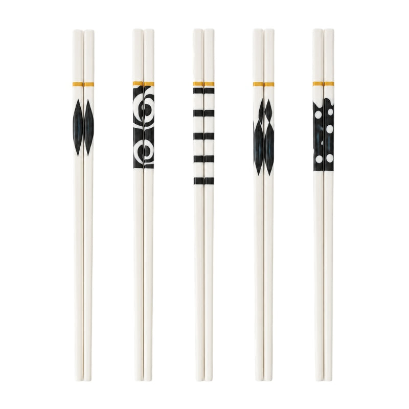 Set of 5 pairs of white ceramic chopsticks with five different black geometric patterns and gold bands, displayed on white background