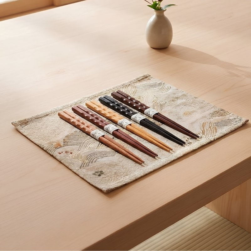 Five pairs of chopsticks in bamboo with carved dot grip banded with Japanese paper rings fanned out on a light wood table near a shoji window