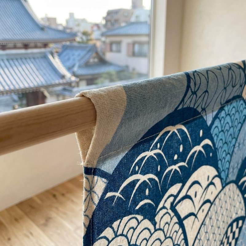 Close-up of curtain japanese noren doorway showing indigo seigaiha wave pattern linen fabric on wooden rod with traditional Kyoto temple rooftop view through window