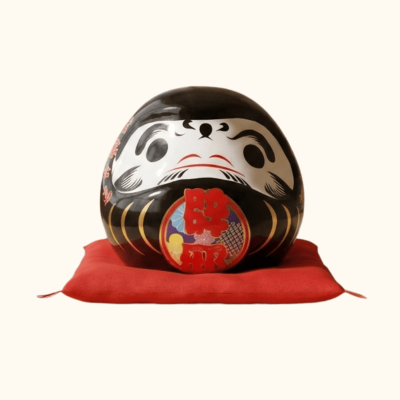 Guardian daruma doll japanese black with vibrant red details displayed on ceremonial red silk cushion against clean white background for clear product view