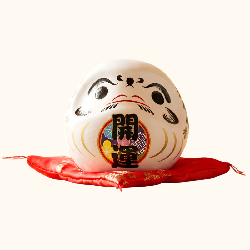 Harmony symbol daruma doll kanji japanese in pure white ceramic with traditional calligraphy details displayed on red floral cushion against cream background