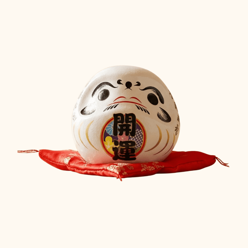 Harmony symbol daruma doll kanji japanese in pure white ceramic with traditional calligraphy details displayed on red floral cushion against white background