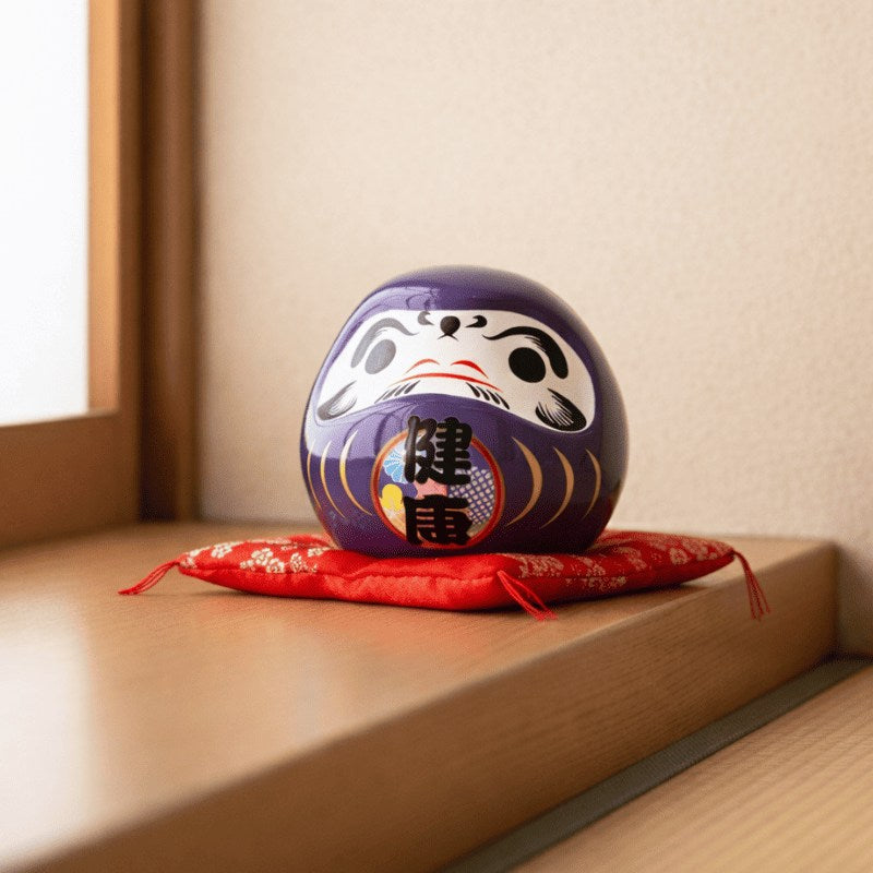 Wellness focused kanji on daruma doll purple in deep purple glaze with health characters sitting on red cushion near wooden shelf with soft natural window light