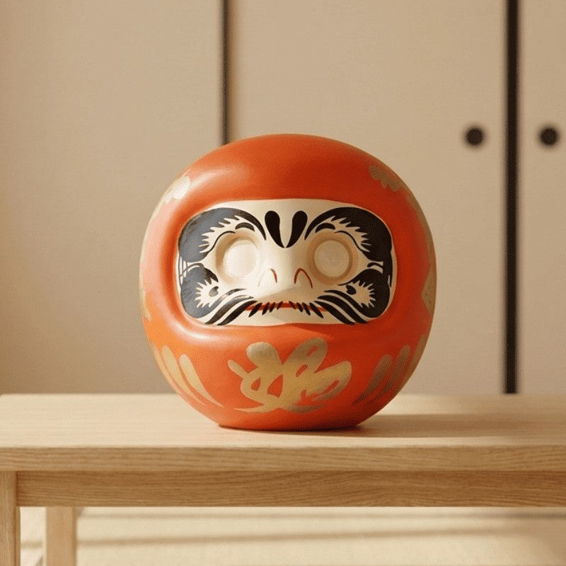 Traditional daruma in Japanese culture displayed in orange glaze on natural wood surface with tatami flooring and sliding paper doors background