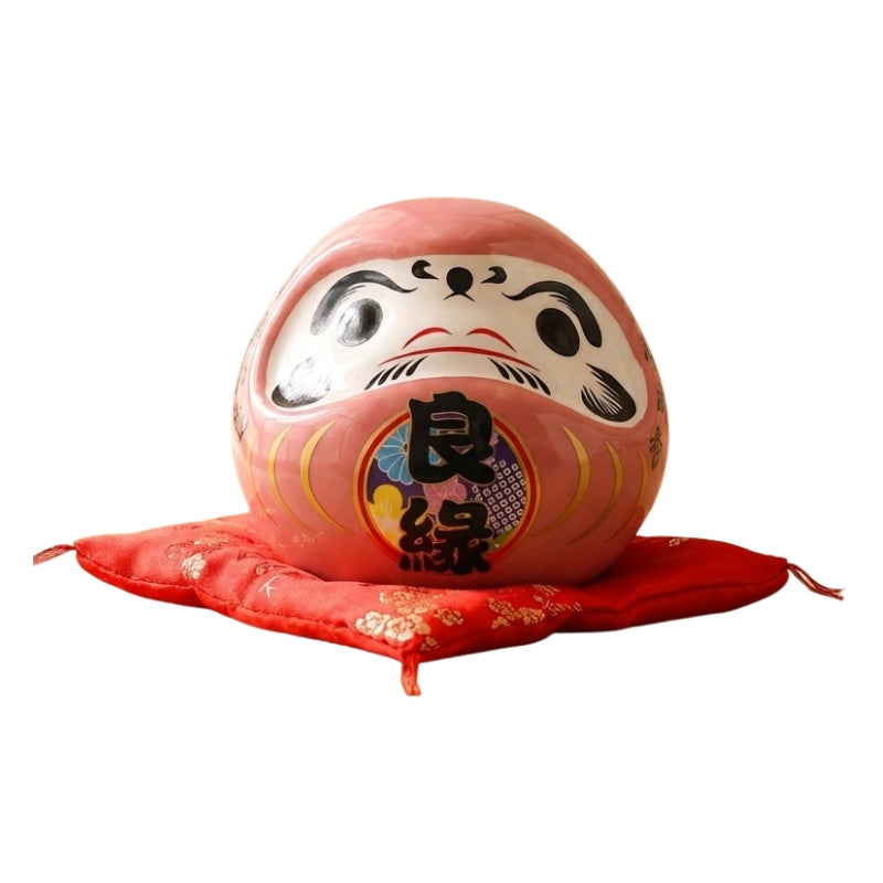 Romantic daruma japanese pink in soft rose ceramic with traditional kanji details displayed on red floral cushion against clean white background view