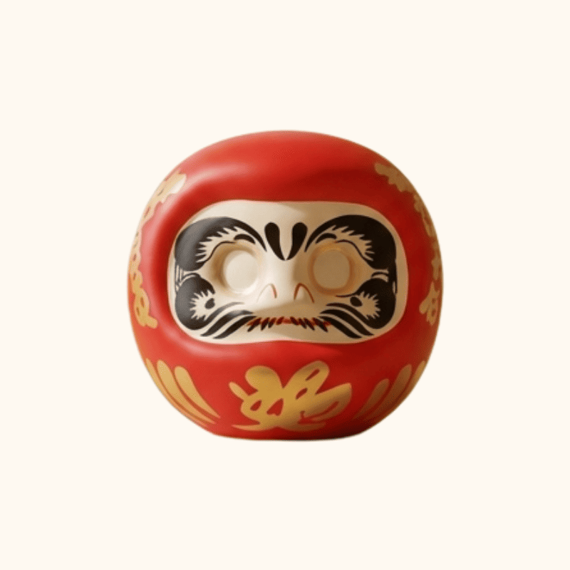 Vibrant red daruma Japanese goal keeper with golden brush accents sitting on minimalist wooden shelf in serene traditional Japanese interior space