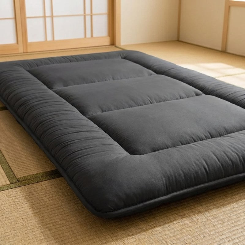 Detail view of futon japanese bed in charcoal gray with padded borders and quilted sections on tatami mat near shoji screens