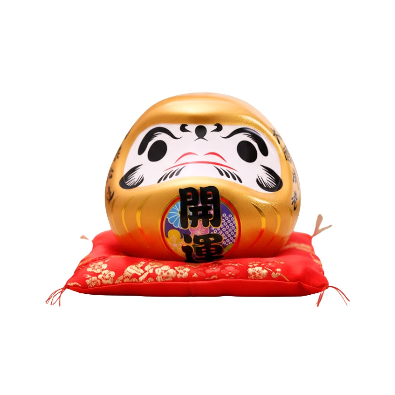 Wealth intention gold japanese daruma in metallic ceramic with prosperity kanji displayed on red floral cushion against clean white background view