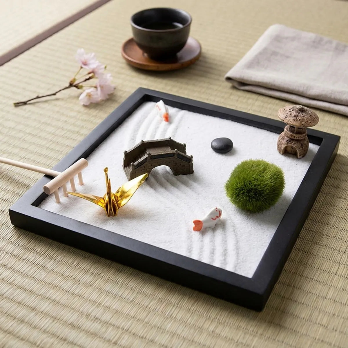 A close view of the curved raked sand lines flowing around the koi figures beside the golden folded origami crane.