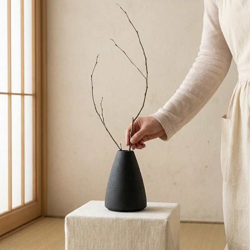 Hand creating minimalist ikebana flower vase arrangement with dried branches near shoji screen window