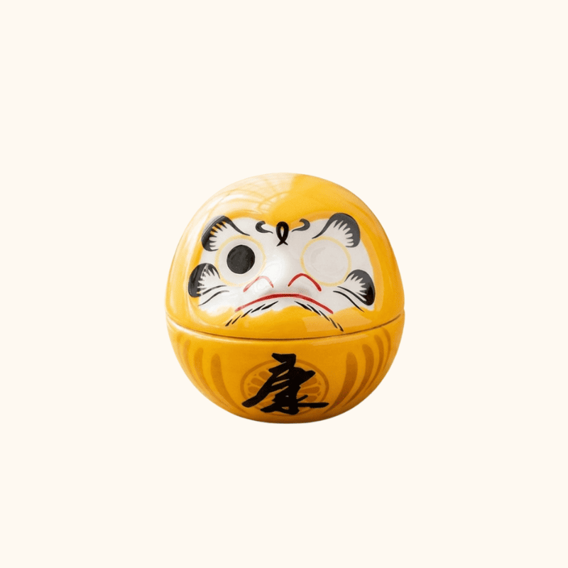 Japanese antique daruma featuring warm yellow glaze and black prosperity character with blank eyes on neutral white backdrop