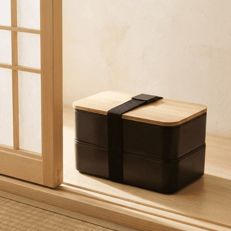 Traditional japanese bento box containers with bamboo top placed on tatami floor beside shoji screen catching soft natural daylight