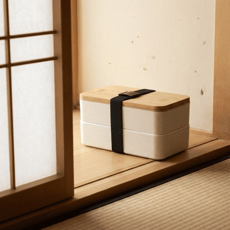 Minimalist white japanese bento box lunches with wood lid positioned on windowsill beside shoji screen catching golden afternoon sunlight