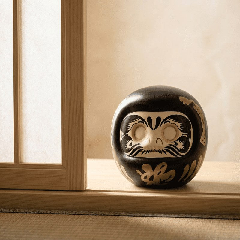Elegant japanese black daruma with golden calligraphy details sits on wooden windowsill catching natural sunlight in Japanese minimalist traditional interior