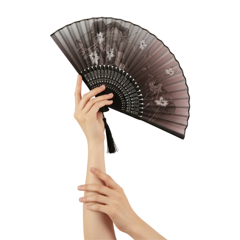 Hands elegantly holding japanese black fan with twilight gradient iris pattern and intricate carved bamboo ribs against white background