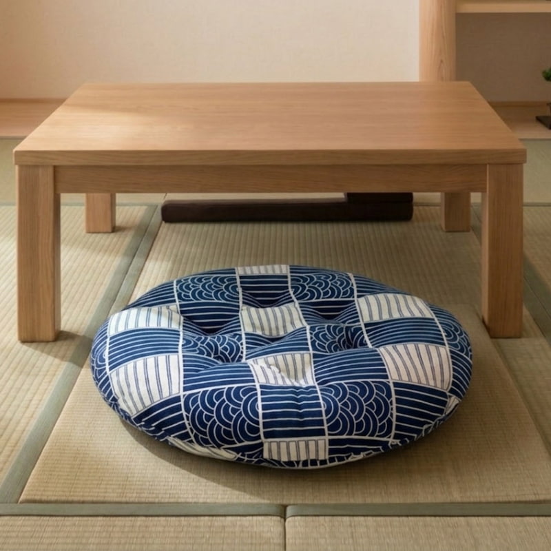 A round floor cushion in Japanese style with a blue wave pattern rests on a wooden floor near a bookshelf