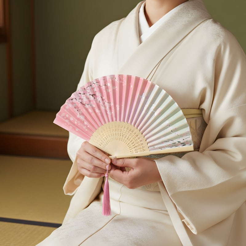 Authentic japanese hand fan with pink cherry blossom design held by person wearing cream kimono in serene traditional tatami room interior