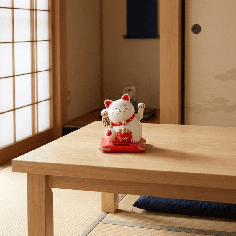 White japanese maneki neko white statue with raised paw and red collar displayed on low wooden table beside shoji screen in traditional tatami room with soft natural light