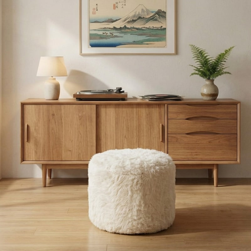 Round Japanese sofa low ottoman in cream faux fur standing on a wood floor in front of a walnut sideboard with turntable, lamp and ceramic vase