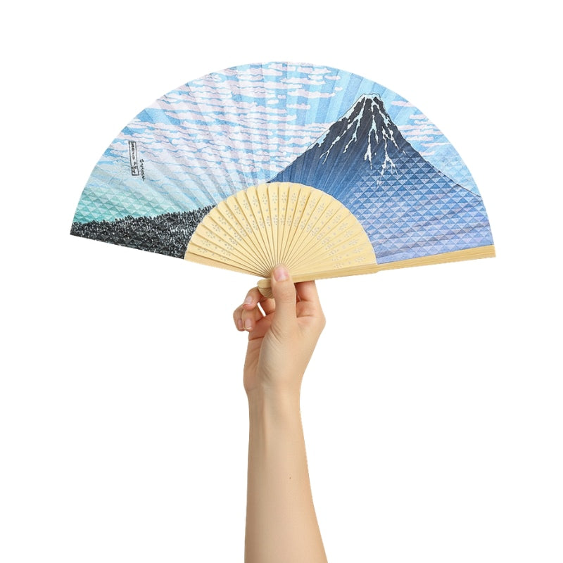Elegant japanese traditional folding fan featuring Mount Fuji and ocean waves held gracefully against white backdrop showcasing detailed blue artwork