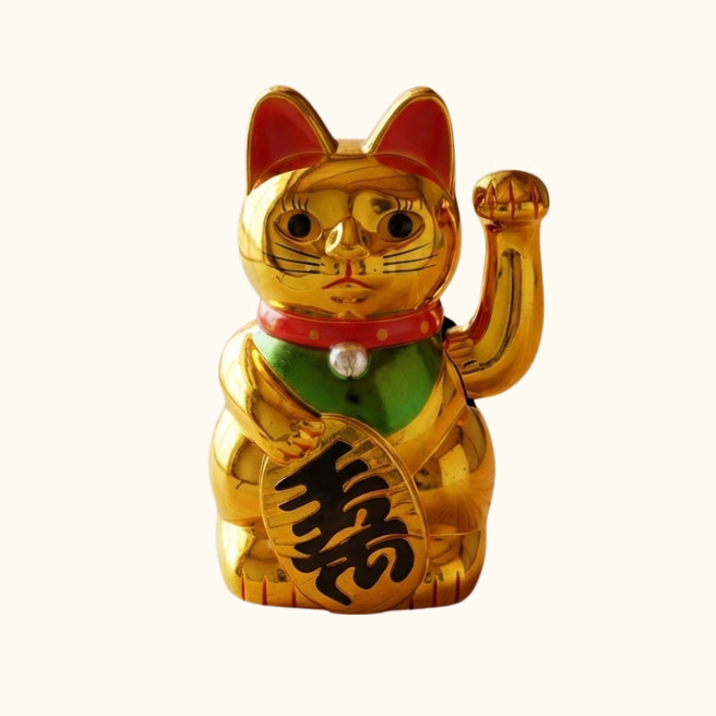 Traditional gold Maneki Neko cat statue with a raised waving paw, green bib and Japanese lucky coin symbolizing good fortune.
