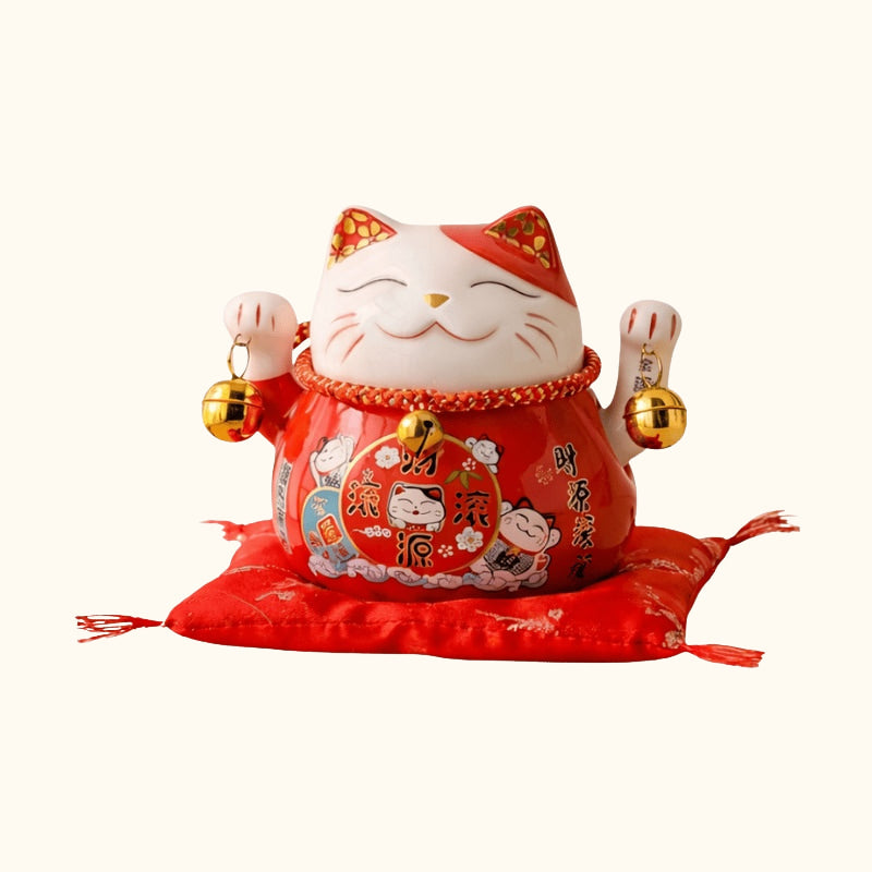 Auspicious maneki neko statue japanese style with prosperity kanji and both welcoming paws raised displayed on red ceremonial cushion against cream