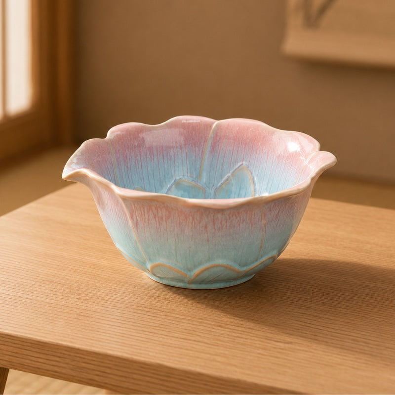 Matcha tea bowl with lotus-shaped scalloped rim and pink-to-turquoise drip glaze on a light wood table in a warm Japanese interior