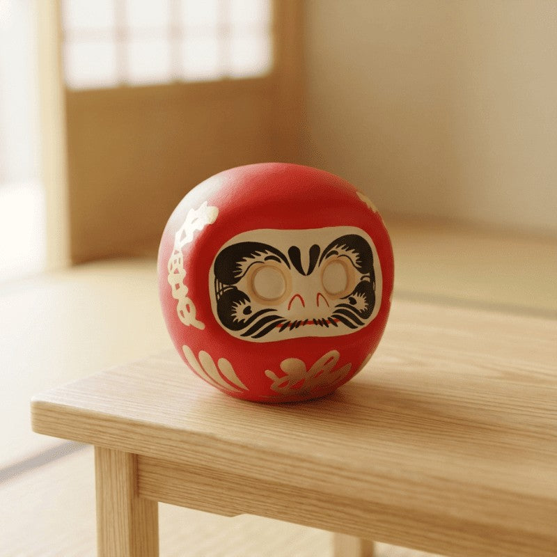 Glossy red daruma Japanese luck symbol with fierce expression and decorative gold patterns isolated on clean white background for clear product view