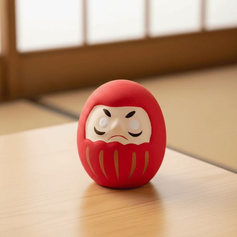 Classic red daruma with determined expression centered on low wooden table in traditional tatami room with sliding paper doors in soft blurred background