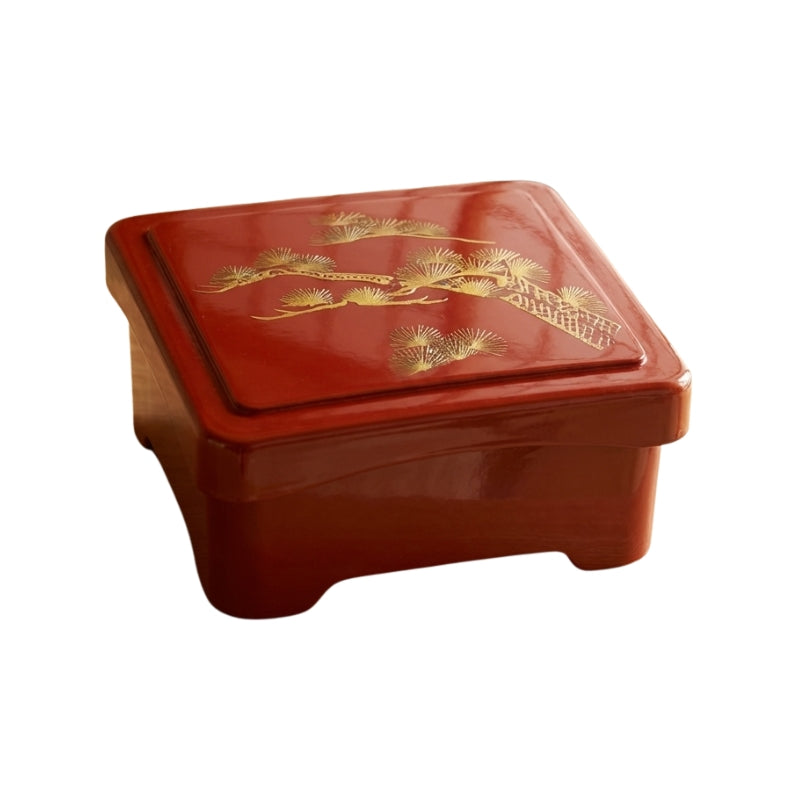 Crimson red sushi bento box with decorative golden pine branches etched on lid against clean white background