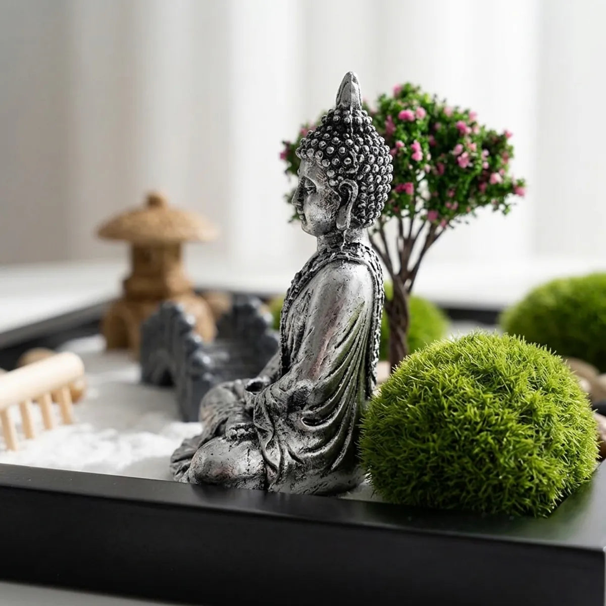 Close-up of the silver Buddha figure's textured robe folds and curled hair beside the bumpy, dense texture of the green moss balls.