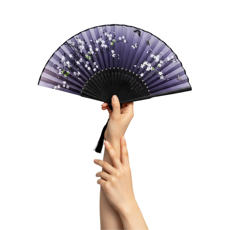 Hand holding vintage fan japanese with purple gradient white cherry blossoms butterfly details and black tassel against clean background