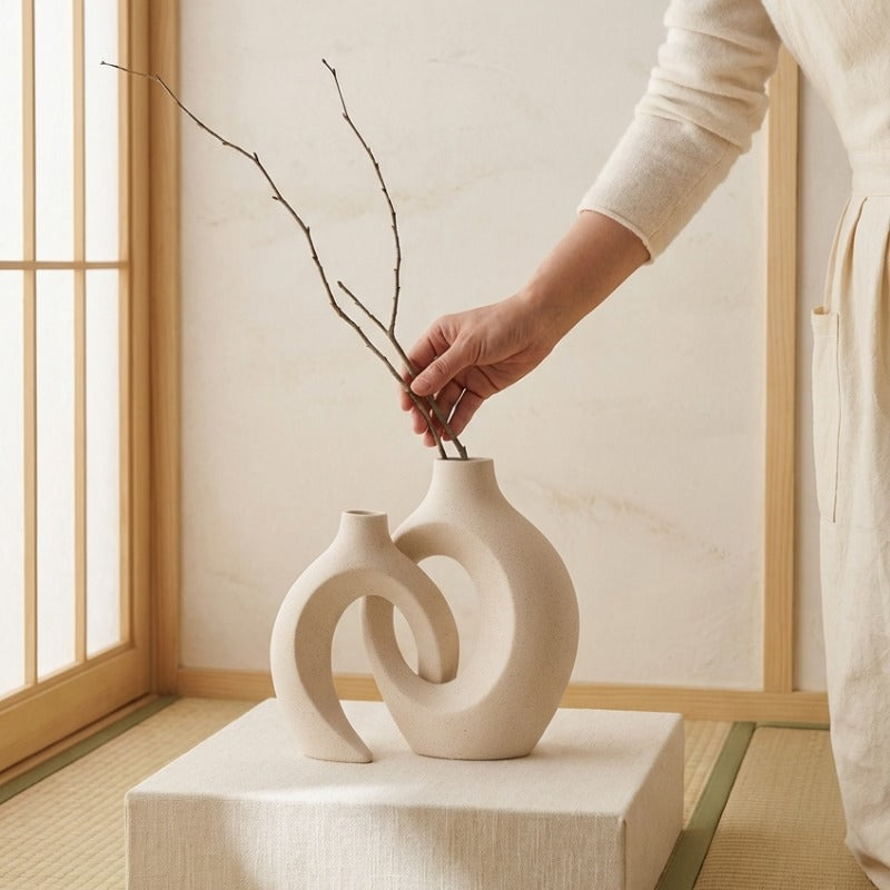 Hand placing branches in artistic vintage white japanese vase displayed on fabric pedestal near tatami