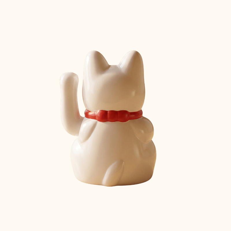 Rear view of a white waving Japanese Maneki Neko cat with a raised paw, red collar and curved tail.