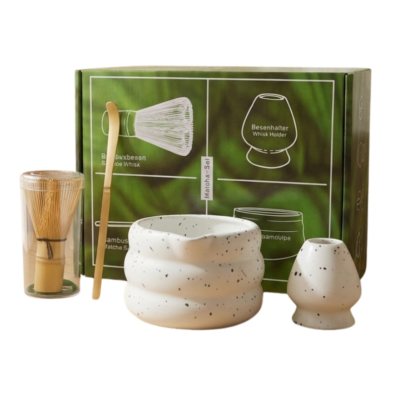 Traditional tea matcha set with speckled ceramic bowl and bamboo accessories displayed with green illustrated gift box on neutral background
