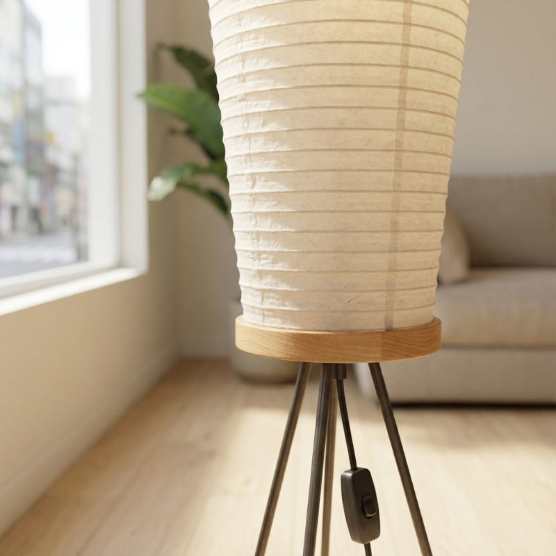 Detail view of akari lamp japanese featuring tall sculptural rice paper cylinder with horizontal pleats and wooden cap on black tripod base
