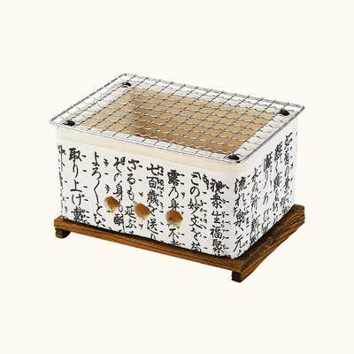 Small Japanese barbecue with white ceramic body covered in black kanji calligraphy and stainless steel mesh grill on a dark wood stand on white background