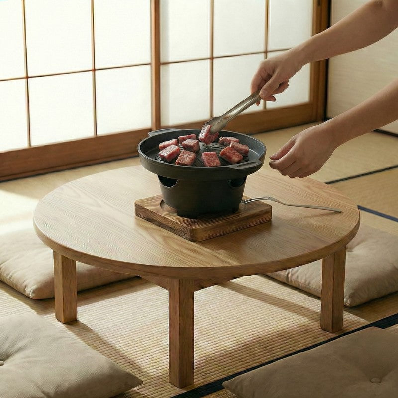 Barbecue style Japanese cooking beef cubes with metal tongs on round low table in traditional tatami mat room
