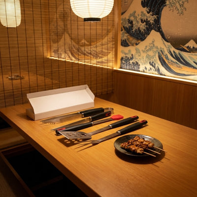 Complete bbq set tool with spatula tongs fork and silicone brush on wooden table in Japanese izakaya with Hokusai Great Wave mural and paper lanterns