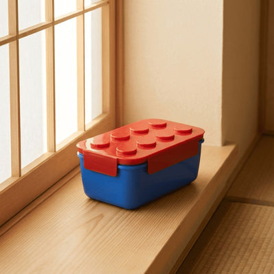 Reversible color bento box japanese big with coral red Lego lid on wooden windowsill beside shoji screen in warm afternoon sunlight