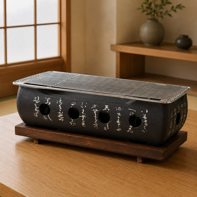 Big Japanese barbecue grill with black ceramic body engraved with white kanji calligraphy and stainless steel cooking grid on a dark wood stand on a wooden table in a traditional Japanese room