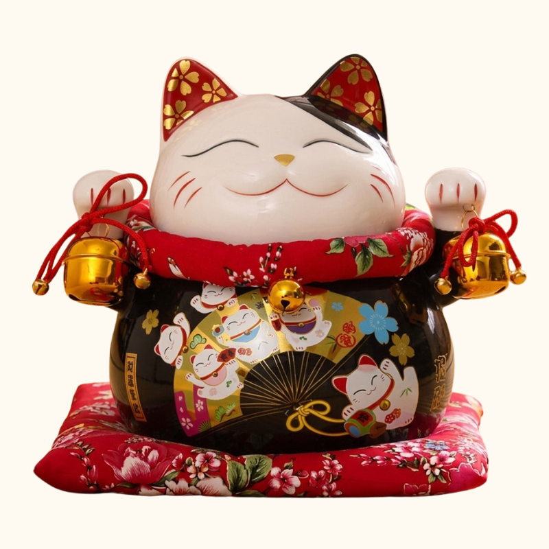 Front view of a big maneki neko black lucky cat statue with a gold folding fan motif on its belly and red floral collar, photographed on a clean studio background