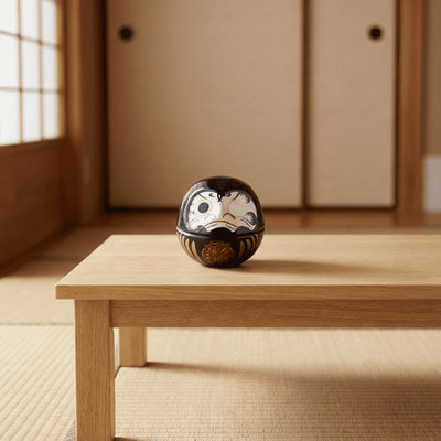 Glossy black daruma mini with red accents and gold prosperity symbol displayed on low wooden table in traditional tatami room