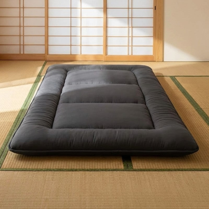 Modern black futon japanese bed with thick quilted borders positioned on tatami floor near shoji screens catching warm natural sunlight