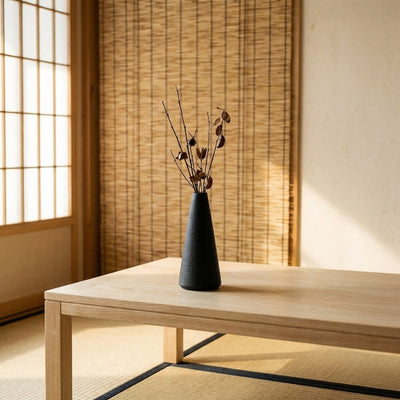 Minimalist black japanese vintage vase with dried branches on wooden table near bamboo blind and shoji screen