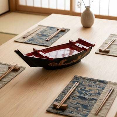 Boat floating sushi black lacquer with red interior and gold wave design on table surrounded by patterned placemats